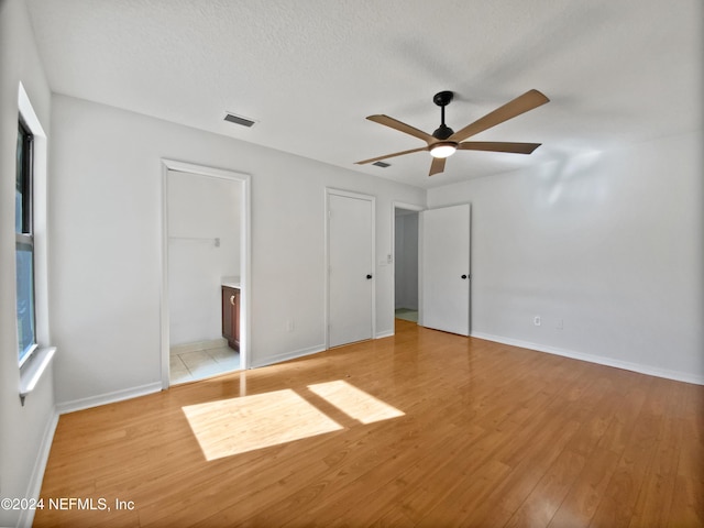 unfurnished bedroom with a textured ceiling, light wood-type flooring, ensuite bathroom, and ceiling fan