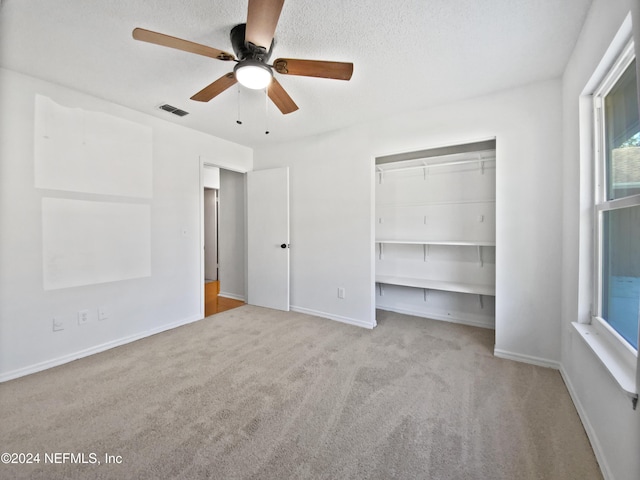 unfurnished bedroom featuring ceiling fan, a closet, light colored carpet, and a textured ceiling