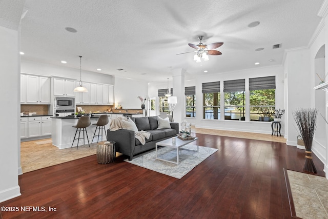 living room featuring wood-type flooring, a textured ceiling, ceiling fan, and crown molding