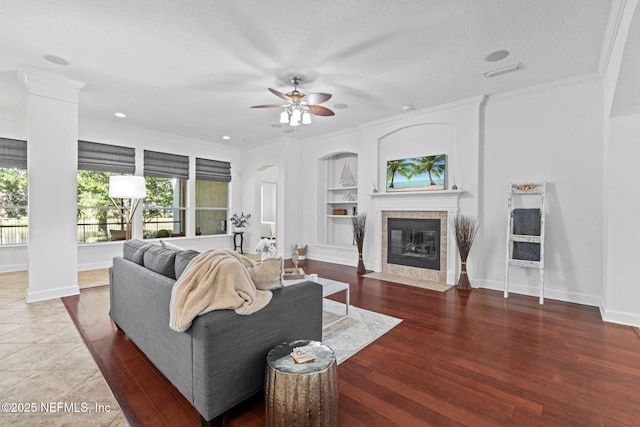 living room with built in shelves, ceiling fan, a textured ceiling, and a tile fireplace