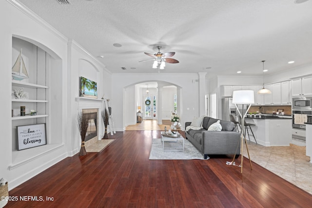 living room featuring ceiling fan, dark hardwood / wood-style floors, ornamental molding, and a textured ceiling