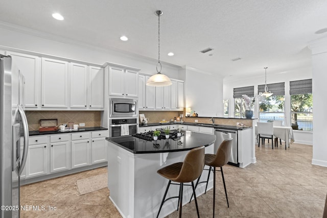 kitchen featuring white cabinets, appliances with stainless steel finishes, backsplash, and hanging light fixtures