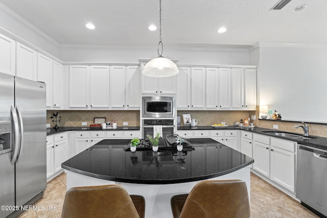 kitchen with appliances with stainless steel finishes, ornamental molding, sink, pendant lighting, and white cabinets