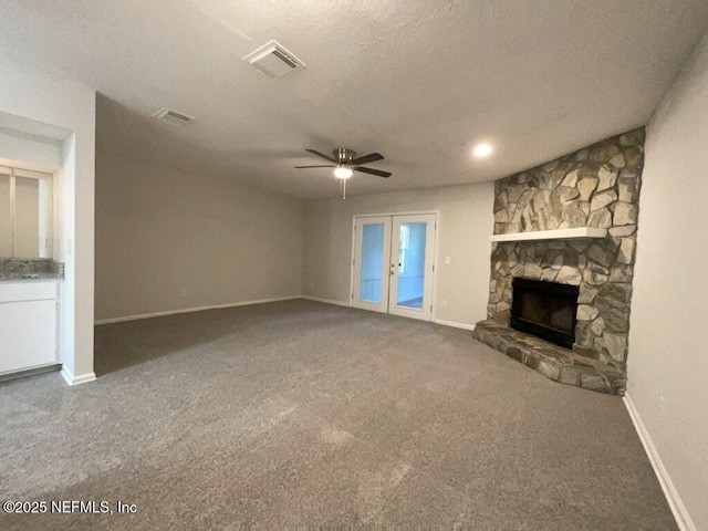 unfurnished living room with french doors, a stone fireplace, a textured ceiling, ceiling fan, and carpet