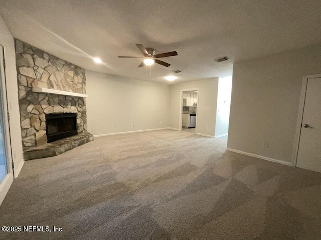 unfurnished living room featuring ceiling fan, a stone fireplace, and carpet