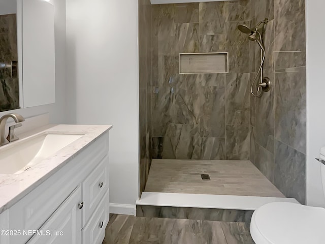 bathroom with tiled shower, vanity, and toilet