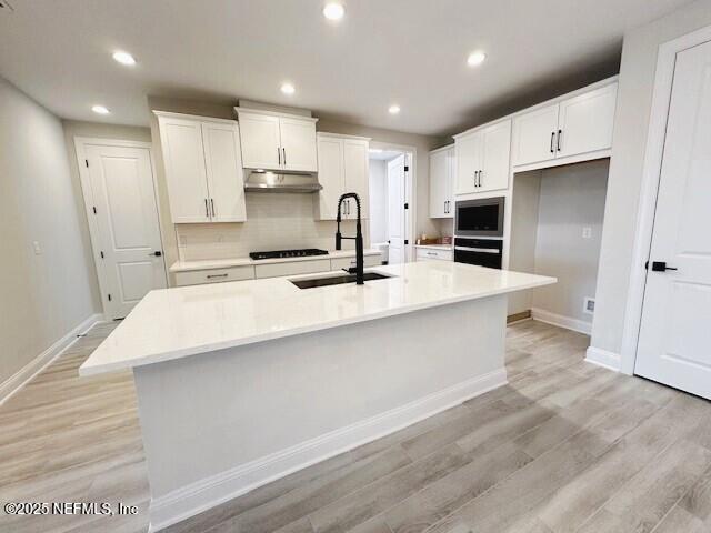 kitchen with a large island, white cabinetry, a sink, under cabinet range hood, and black appliances