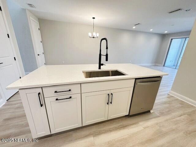 kitchen with a sink, light countertops, light wood-type flooring, dishwasher, and an island with sink