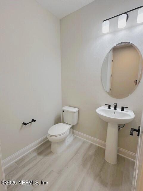 half bath featuring a sink, toilet, baseboards, and wood finished floors