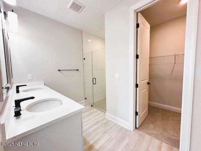 bathroom with a stall shower, visible vents, wood finished floors, a walk in closet, and a sink