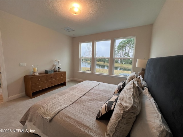 bedroom with light carpet, a water view, a textured ceiling, and baseboards