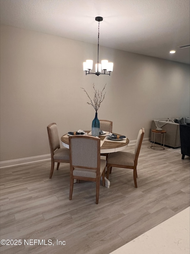 dining space featuring light wood finished floors, baseboards, and a chandelier