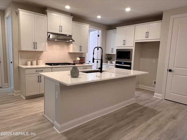 kitchen featuring light wood-style flooring, stainless steel microwave, under cabinet range hood, gas cooktop, and a sink