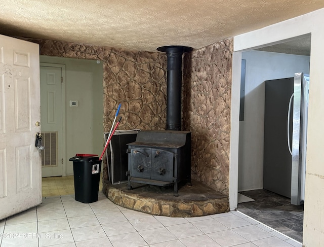 interior details featuring stainless steel fridge, a wood stove, and a textured ceiling