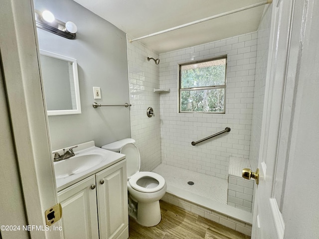 bathroom featuring tiled shower, vanity, hardwood / wood-style flooring, and toilet