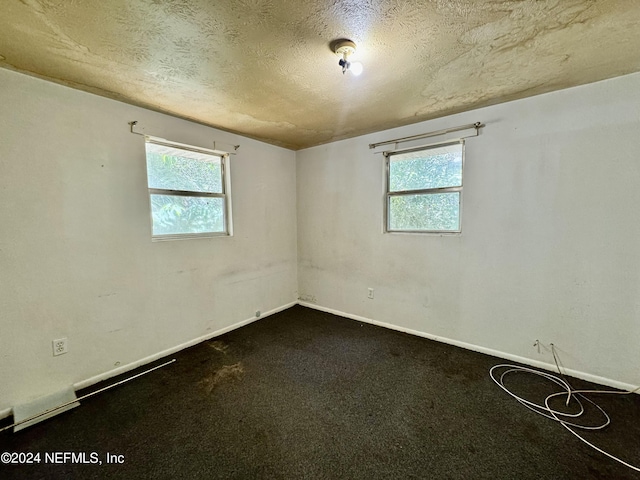 spare room with a textured ceiling and dark colored carpet