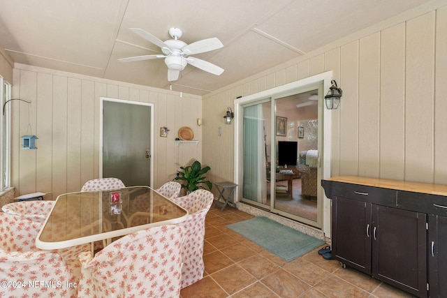 dining room featuring tile patterned floors, wooden walls, and ceiling fan