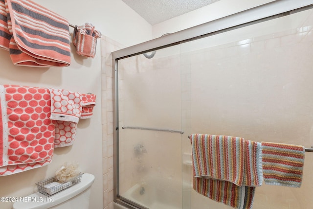 bathroom with combined bath / shower with glass door, a textured ceiling, and toilet