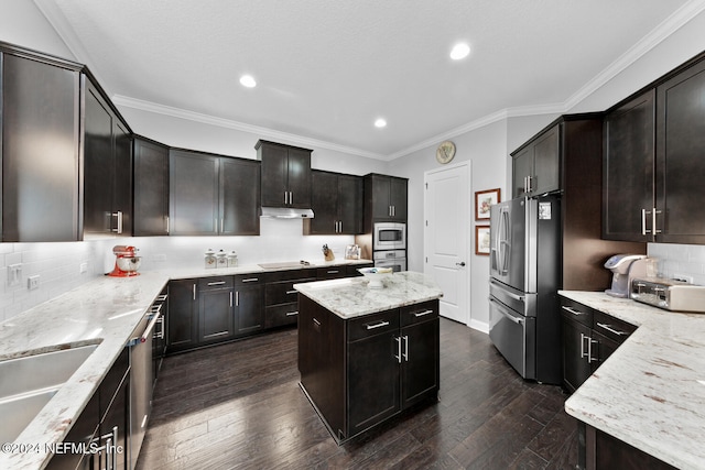 kitchen with appliances with stainless steel finishes, dark hardwood / wood-style flooring, light stone counters, ornamental molding, and a kitchen island