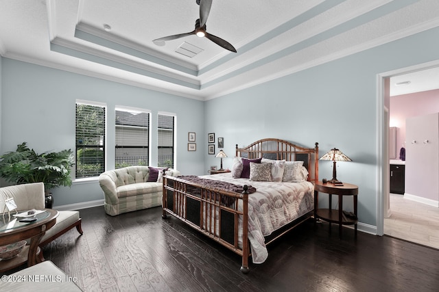 bedroom featuring crown molding, ensuite bath, dark hardwood / wood-style floors, ceiling fan, and a tray ceiling