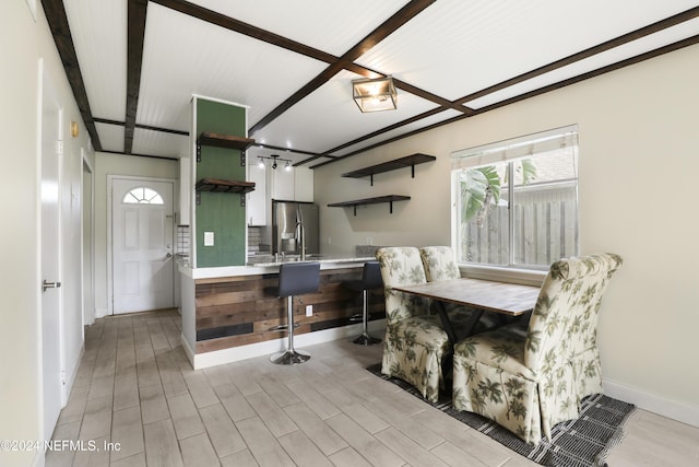 dining area featuring beamed ceiling, light hardwood / wood-style flooring, and sink