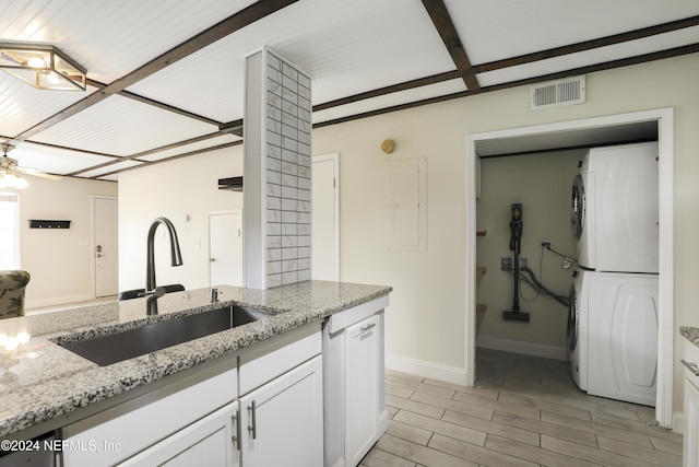 kitchen with white cabinetry, light stone countertops, stacked washing maching and dryer, and sink