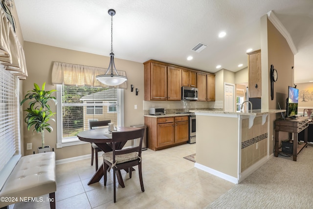 kitchen with kitchen peninsula, appliances with stainless steel finishes, a kitchen breakfast bar, decorative light fixtures, and light tile patterned flooring