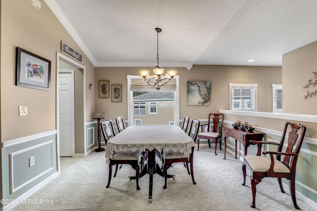 dining room featuring an inviting chandelier, vaulted ceiling, ornamental molding, a textured ceiling, and light colored carpet