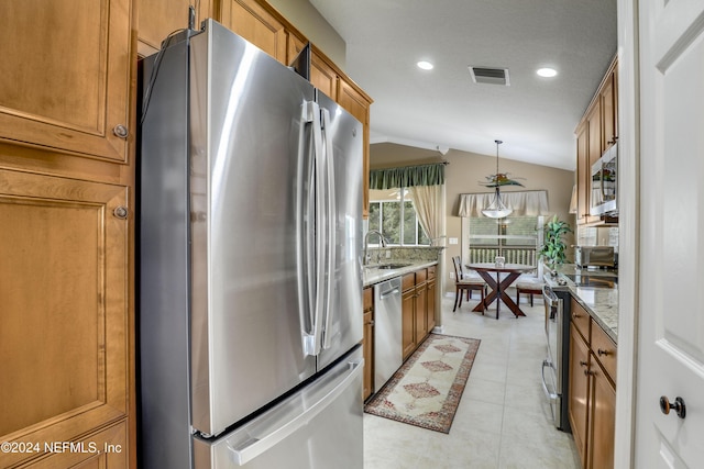 kitchen featuring light stone countertops, appliances with stainless steel finishes, sink, hanging light fixtures, and lofted ceiling