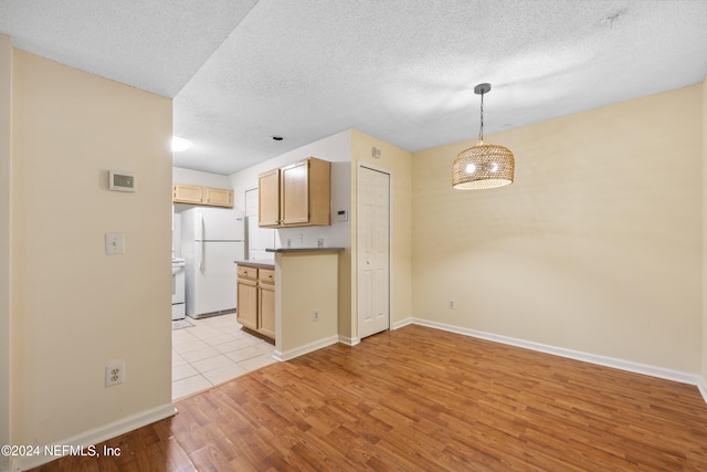 kitchen with white refrigerator, a textured ceiling, light brown cabinetry, decorative light fixtures, and light hardwood / wood-style floors