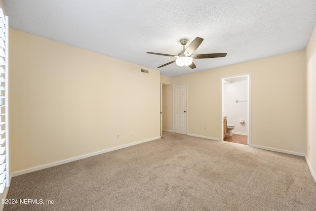 unfurnished bedroom featuring a textured ceiling, light colored carpet, ensuite bath, and ceiling fan