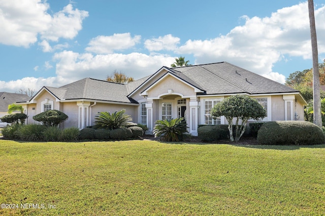 view of front of home with a shingled roof, a front lawn, and stucco siding