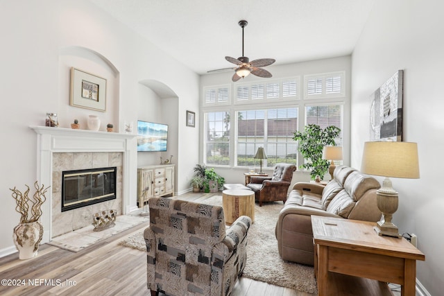 living area featuring a ceiling fan, a fireplace, baseboards, and wood finished floors