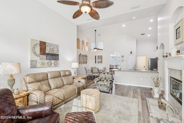 living room featuring high vaulted ceiling, wood finished floors, a fireplace, and ceiling fan with notable chandelier