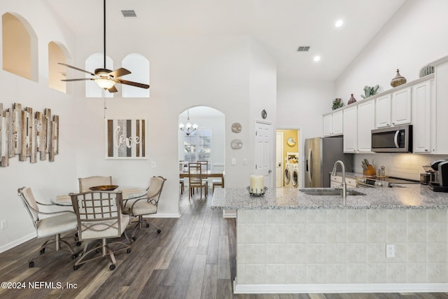 kitchen featuring arched walkways, dark wood finished floors, stainless steel appliances, white cabinetry, and a sink