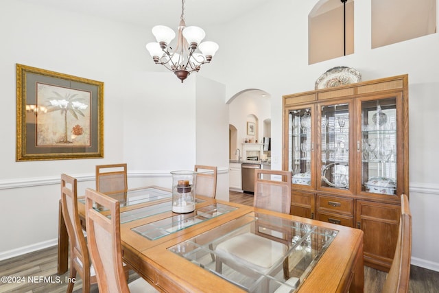 dining area featuring arched walkways, baseboards, wood finished floors, and a chandelier