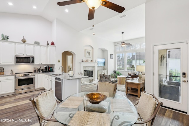 dining space with high vaulted ceiling, light wood-type flooring, a glass covered fireplace, and visible vents