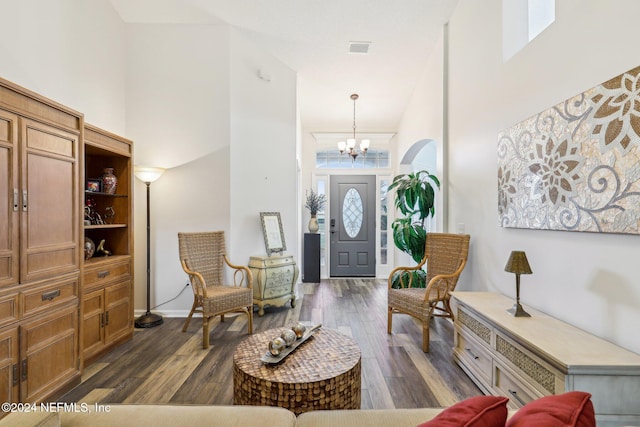 entrance foyer featuring dark wood-style flooring, a notable chandelier, visible vents, a high ceiling, and baseboards