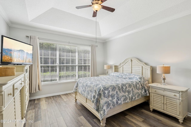 bedroom with a raised ceiling, crown molding, baseboards, and wood finished floors