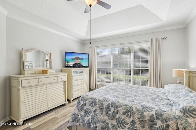 bedroom featuring light wood-type flooring, a tray ceiling, and ornamental molding