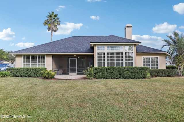 back of property featuring a lawn, a chimney, a sunroom, and stucco siding