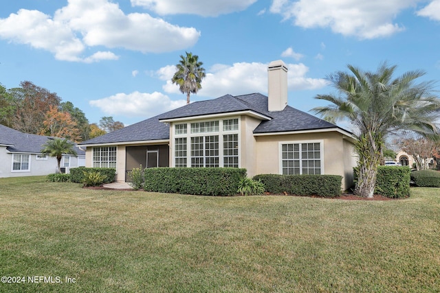 rear view of property featuring roof with shingles, a yard, a chimney, and stucco siding