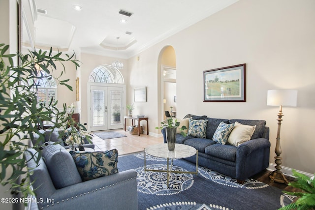 living room featuring visible vents, tile patterned floors, crown molding, baseboards, and arched walkways