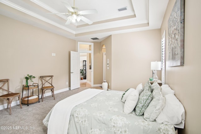 carpeted bedroom with visible vents, baseboards, arched walkways, crown molding, and a raised ceiling