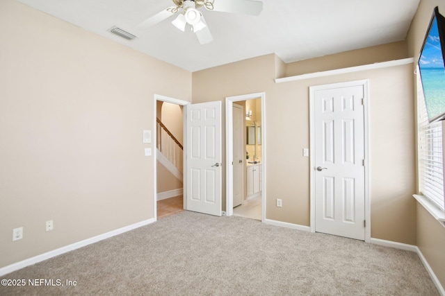 unfurnished bedroom featuring baseboards, visible vents, carpet floors, ensuite bath, and ceiling fan