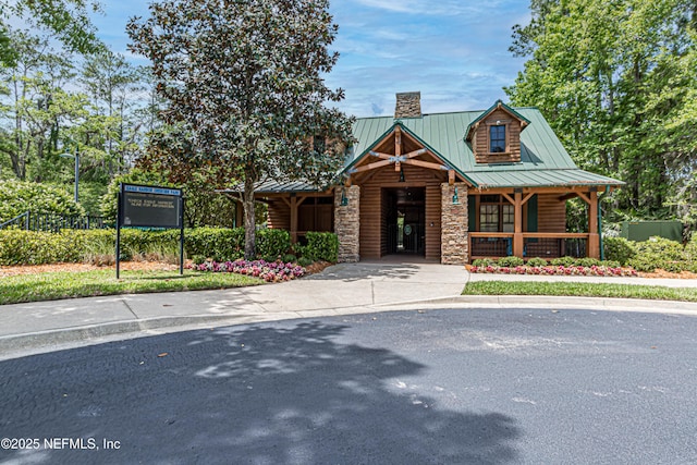 view of front of home with metal roof, stone siding, a porch, and a chimney