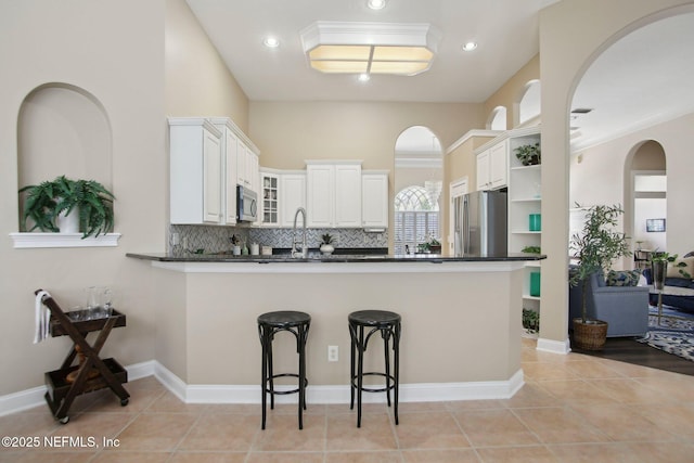 kitchen featuring dark countertops, light tile patterned floors, a peninsula, stainless steel appliances, and open shelves