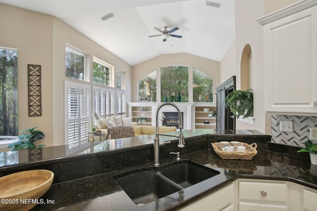 kitchen featuring vaulted ceiling, dark stone countertops, backsplash, and a sink