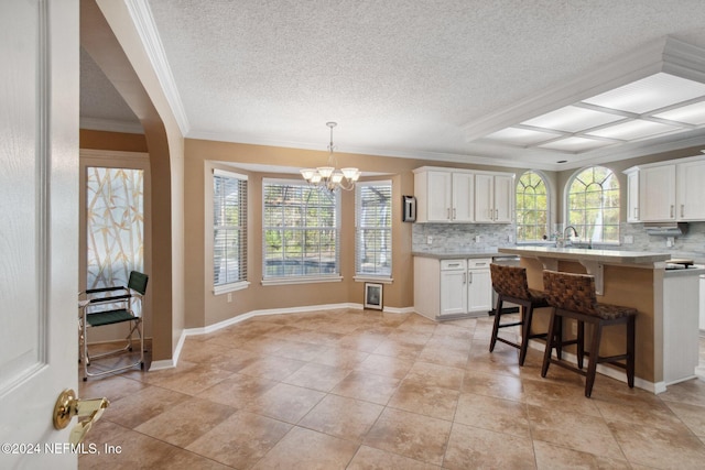 kitchen featuring white cabinetry, hanging light fixtures, backsplash, crown molding, and a kitchen bar