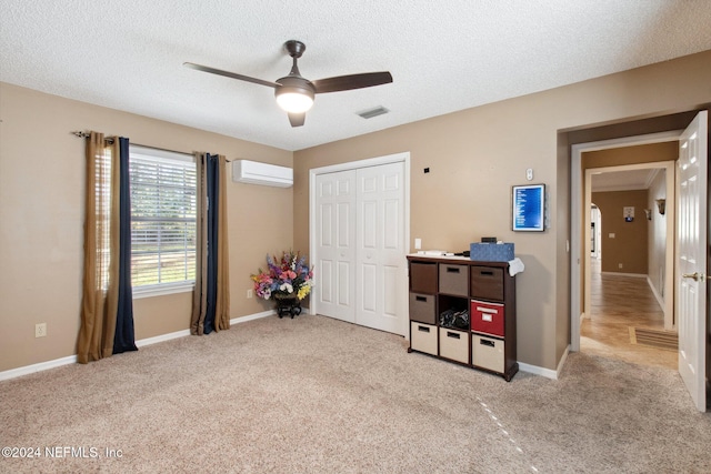 carpeted bedroom with a wall mounted AC, a textured ceiling, a closet, and ceiling fan